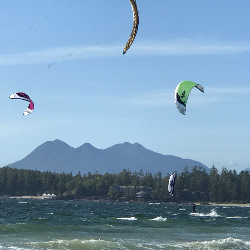 Wind surfers with blue skies, trees and mountains in background