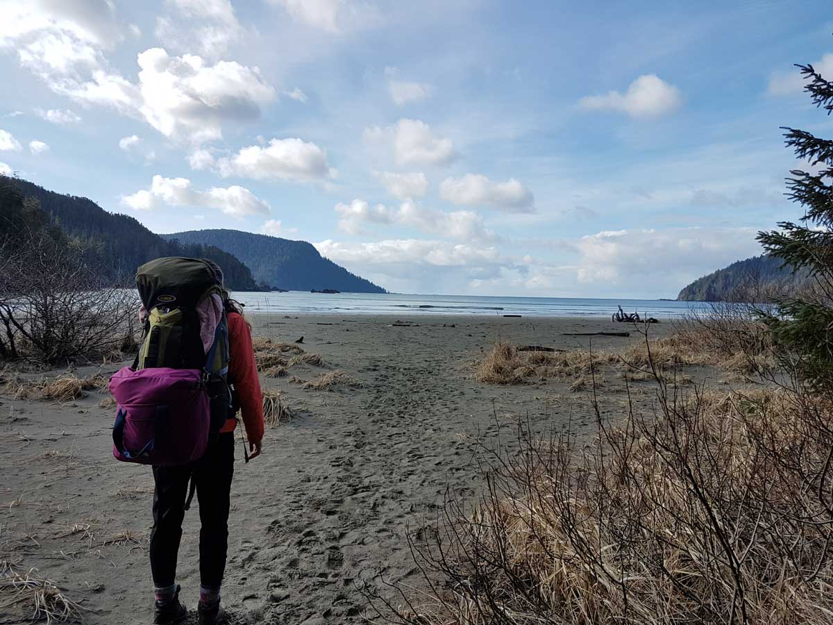 Woman with backpack on beach looking at ocean while visiting Vancouver Island